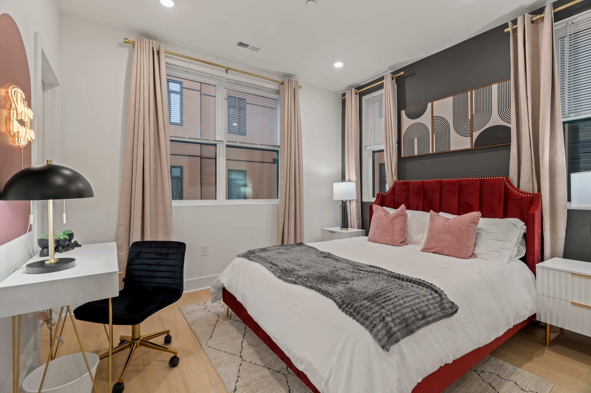 Bedroom with red upholstered headboard, desk, and large windows