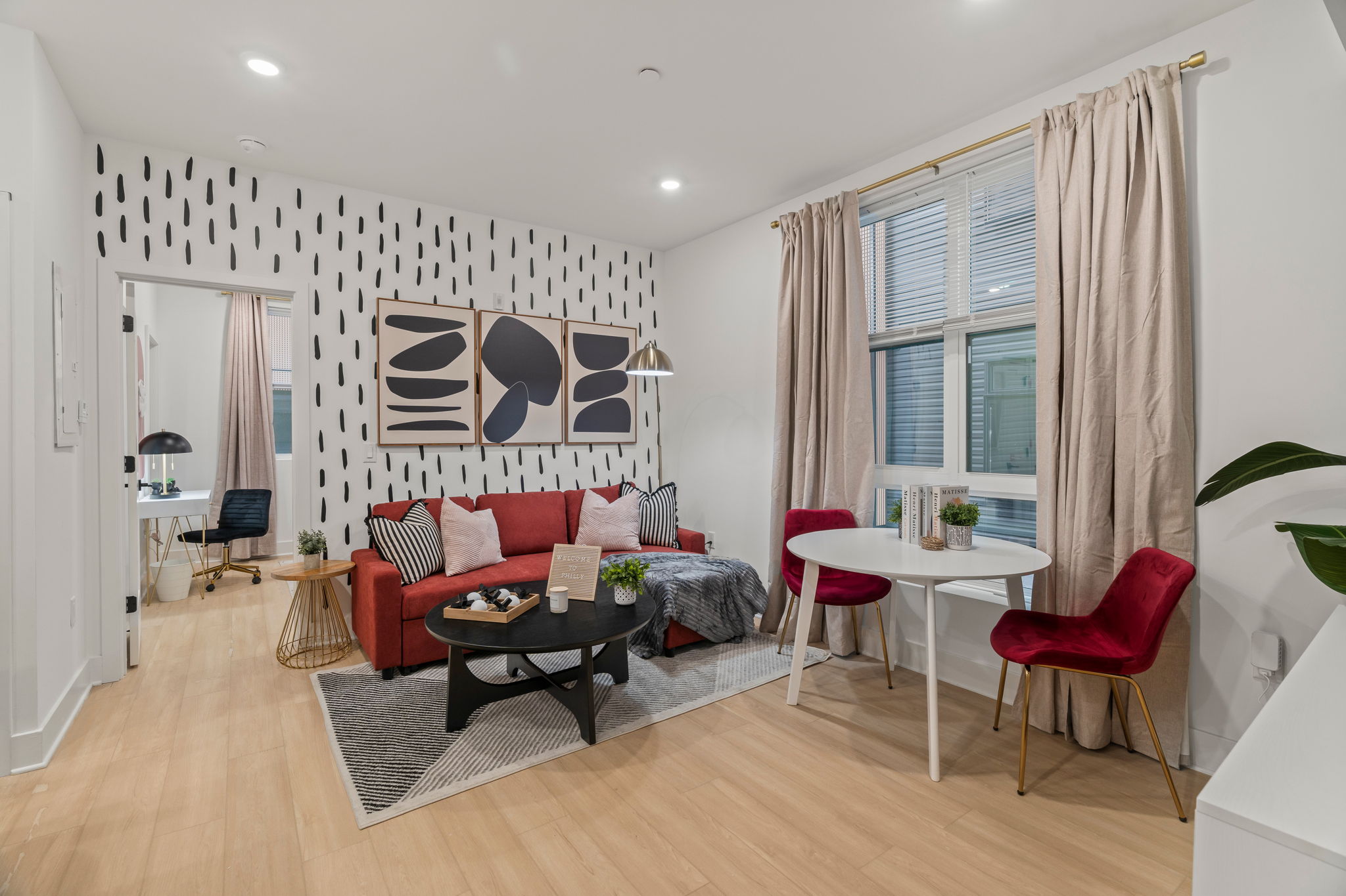 Living room with red sofa, patterned accent wall, and round dining table by the window