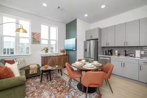 Open living and dining area with green sectional, round table, and gray kitchen cabinets